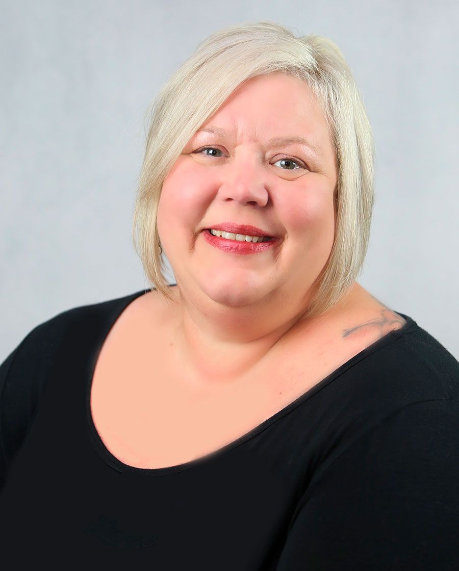 smiling portrait of kristi. she has short very blond hair and is wearing a black scoop neck blouse