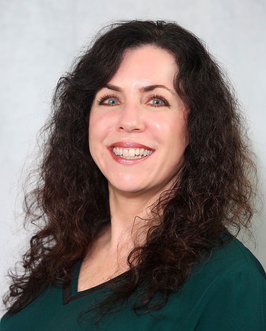 smiling portrait of lisa. she has long wavy brown hair and is wearing a dark greenblouse